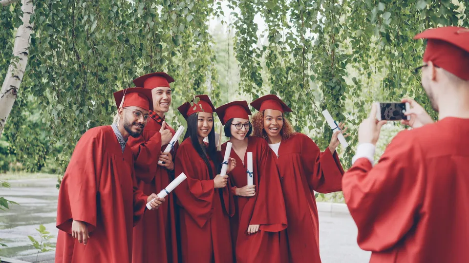 Graduates in red gowns posing for a photo with diplomas